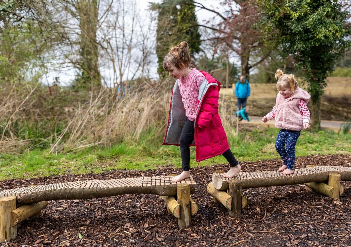 Two young children walking along a balance beam with bare feet