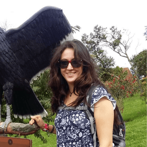A person stands next to a statue of a bird with a grassy landscape behind them