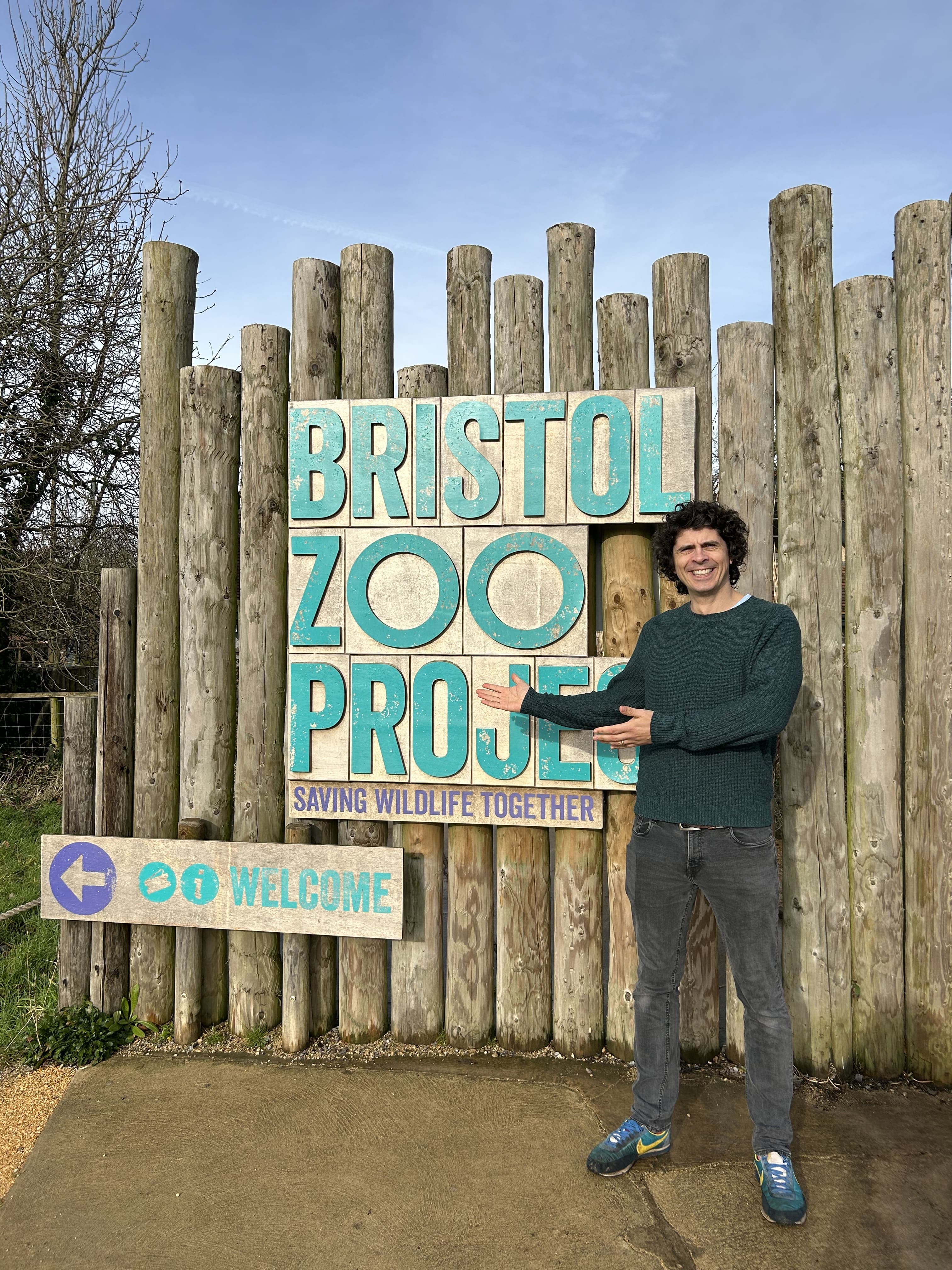 Andy Day standing in front of the wooden Bristol Zoo Project sign at the entrance of the zoo
