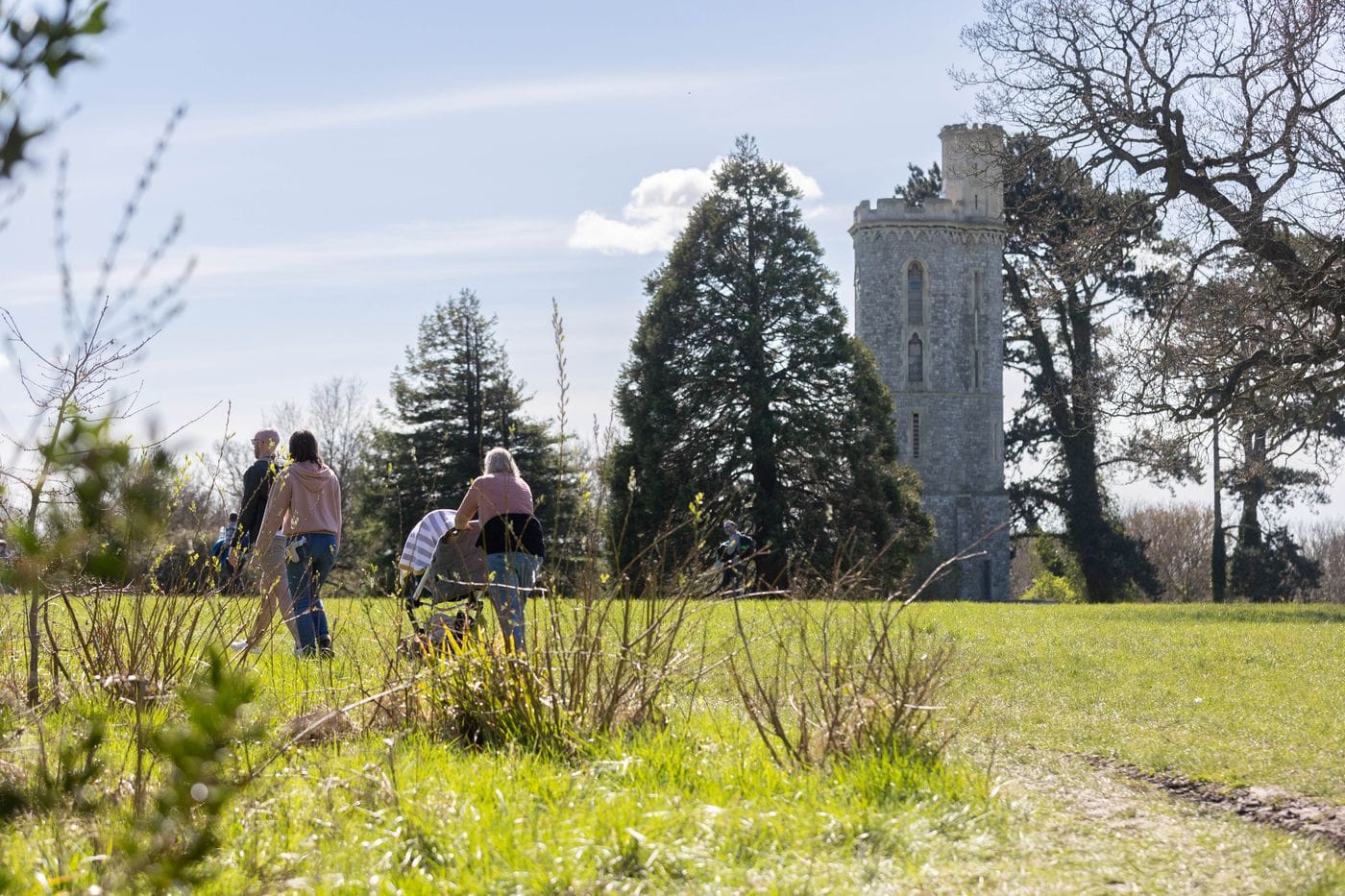 A group of people with a push chair are walking in tower meadow. The tower is seen in the background.